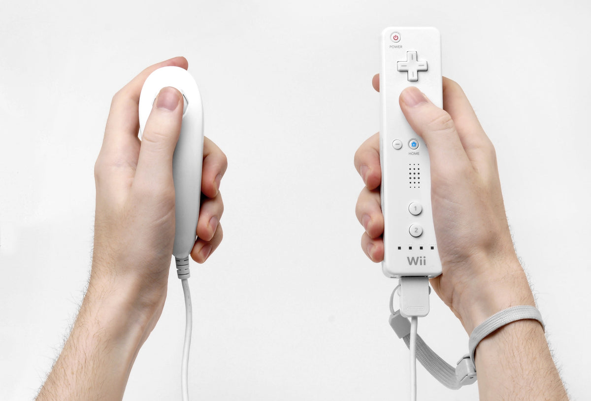 Hands hold an original Wii Remote and Nunchuk with the wrist strap attached